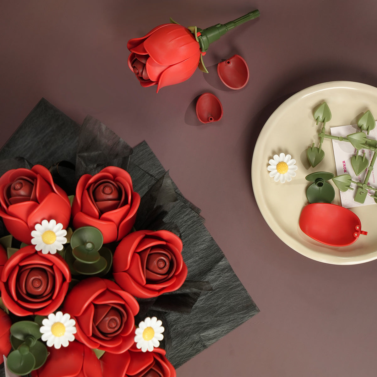 ROKR Red Rose Bouquet DIY kit AF02J flat-lay overhead view of red roses and white daisies with black tissue wrap beside a plate of unassembled red and green plastic parts