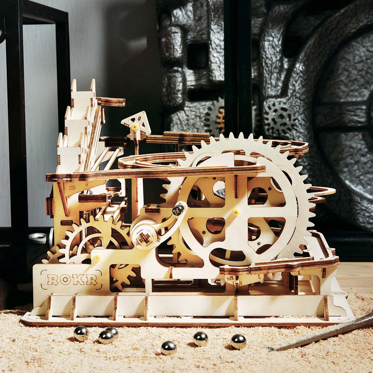 ROKR wooden marble run close-up showing large gear wheel and scattered steel marbles on a sandy display surface