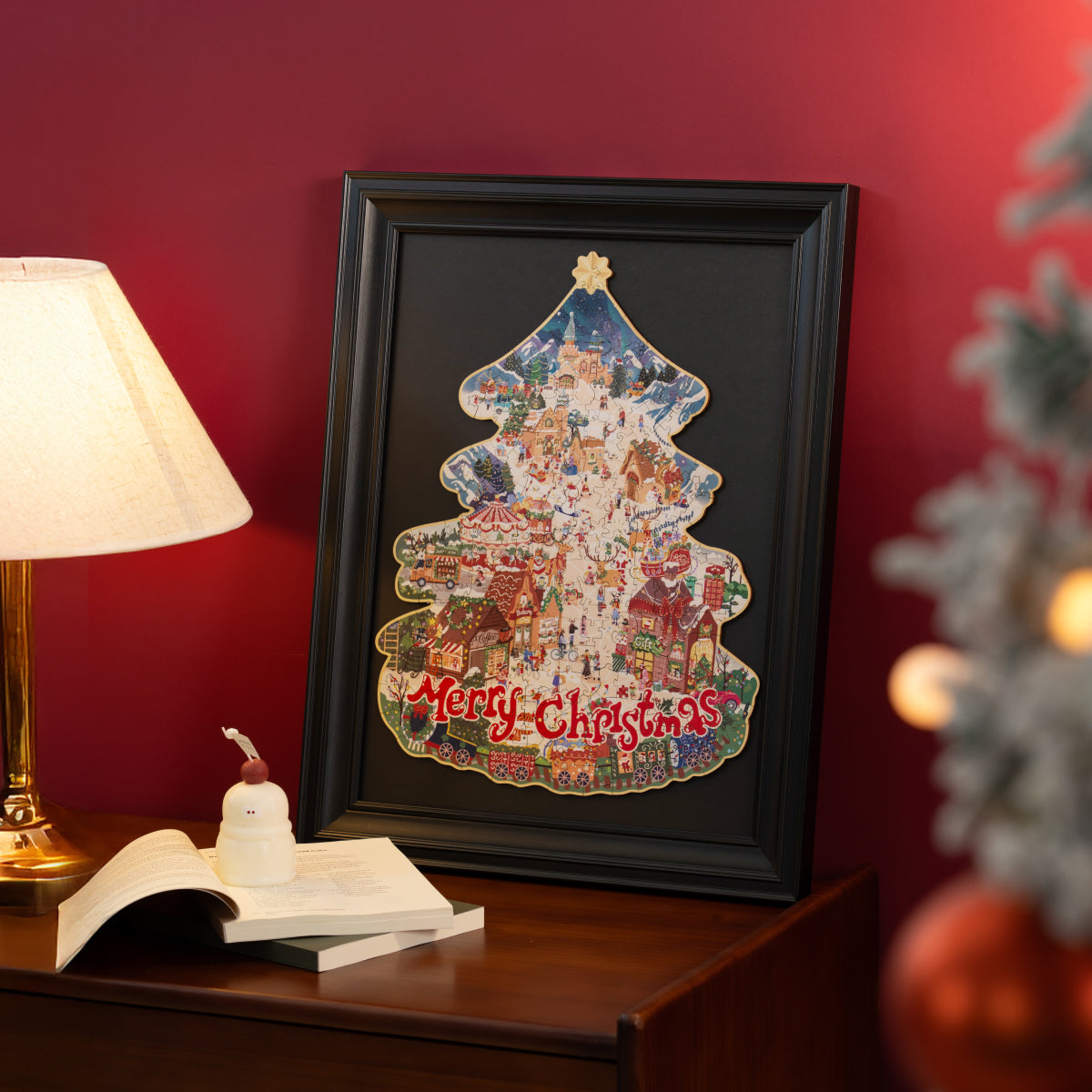 Rowood Christmas Town TA007 puzzle completed and framed in black frame on wooden nightstand beside lamp and Christmas tree
