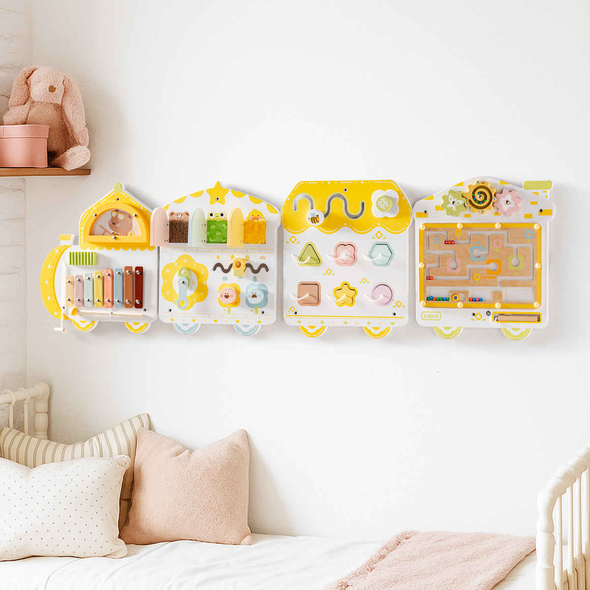 ROBUD yellow and white spring train busy board with four activity panels, mounted on a nursery wall above a cozy cream crib.