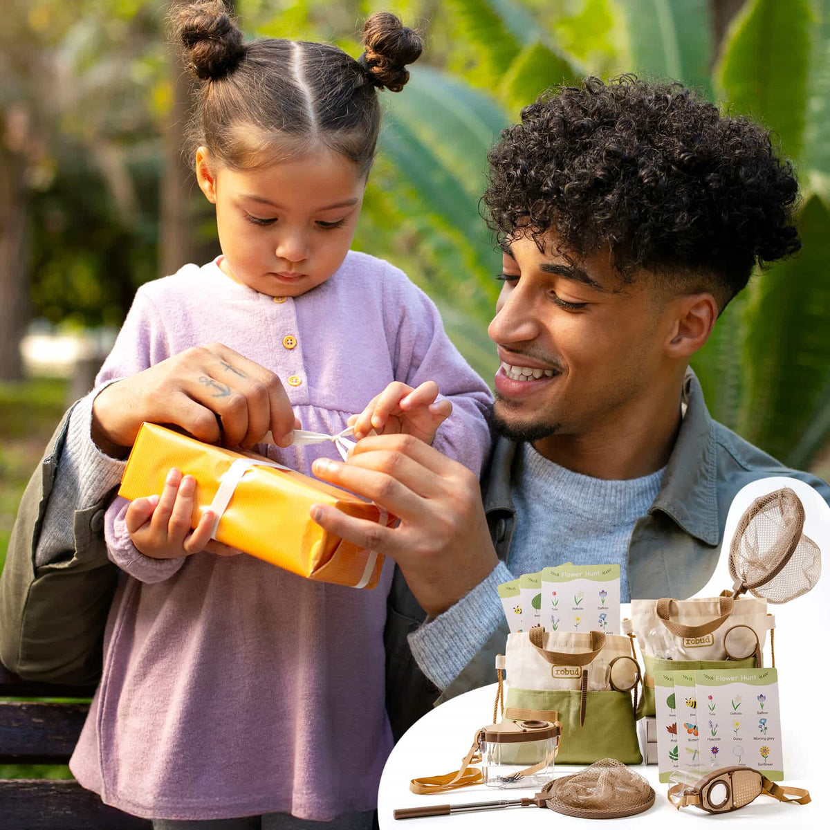 Father smiling and helping young daughter unwrap a yellow gift box with the ROBUD dual explorer kit display visible below