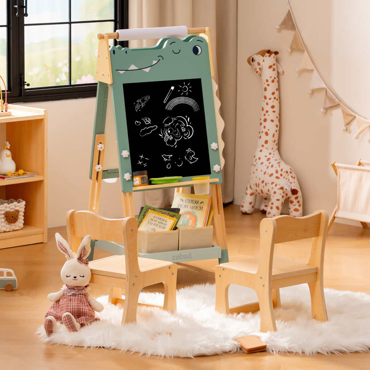 ROBUD green dino chalkboard easel displaying chalk drawings in a stylised kids room alongside a bookcase and chair.