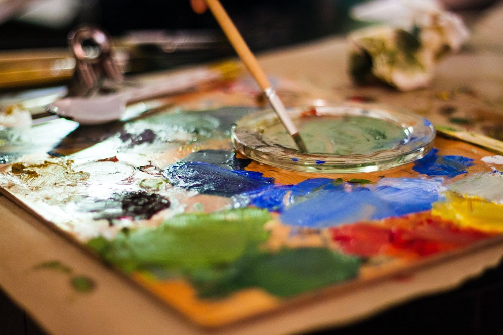 Robotime paint palette holds mixed bright colors and a brush on a messy craft table.