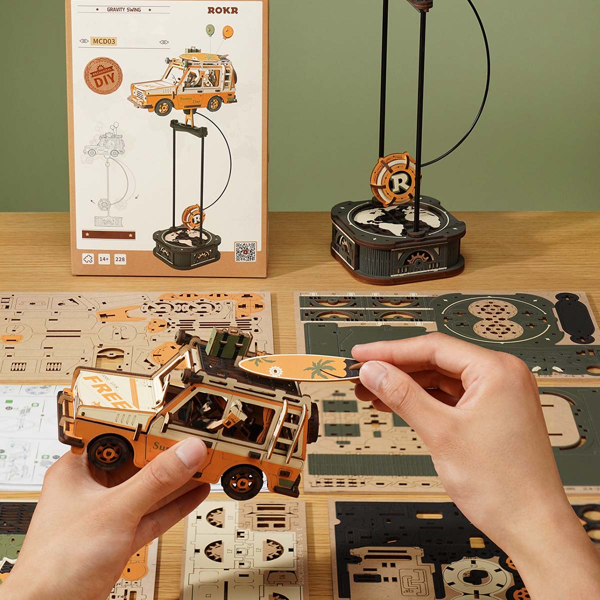 ROKR Road Tripper MCD03 lifestyle showing the orange wooden SUV displayed on the pendulum stand beside a photo frame on a warm desk
