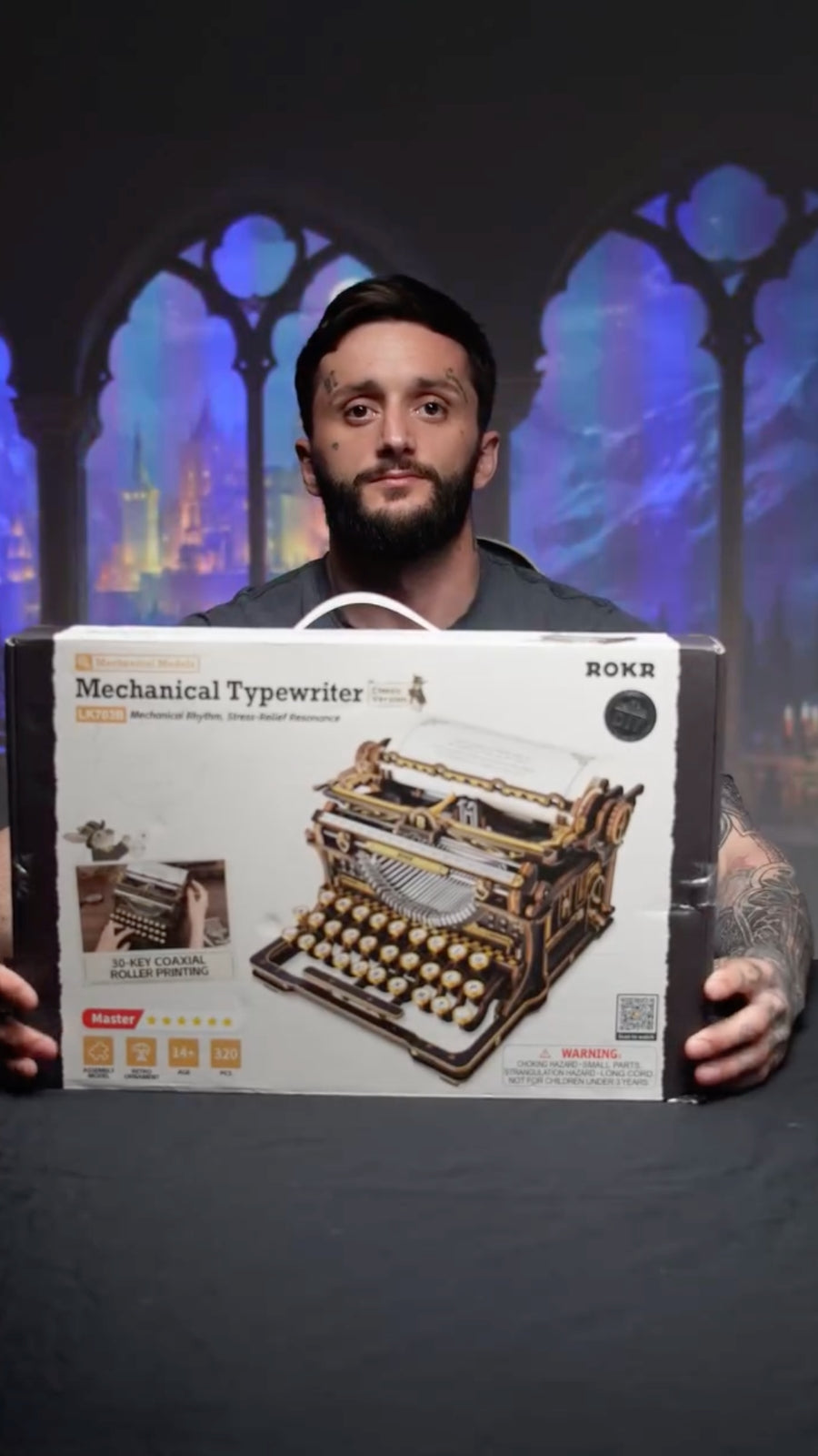 Man presenting a ROKR mechanical typewriter kit box against blue arched windows
