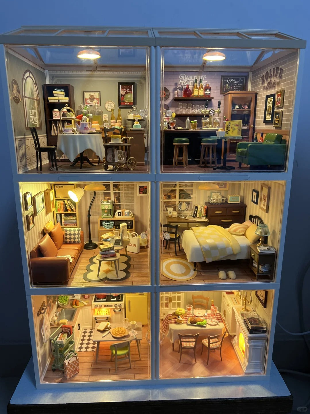 Rolife Super Creator DIY miniature house open front showing six warmly lit rooms with living, kitchen and bedroom dioramas