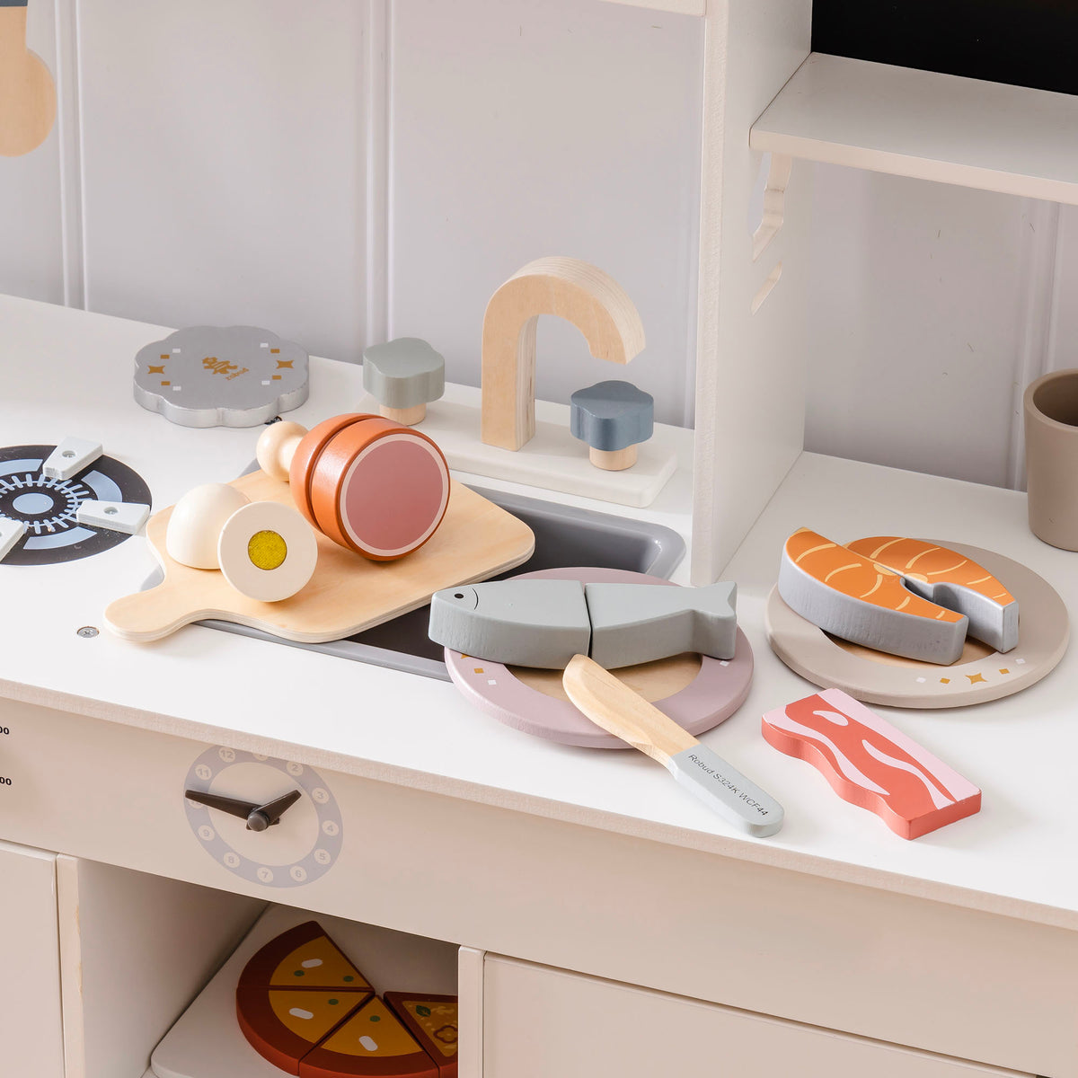 ROBUD wooden meat cutting set arranged on a white play kitchen counter with salmon steak on plate, egg, chicken leg, bacon, grey fish, and wooden knife
