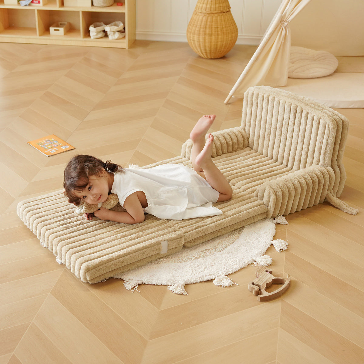Young girl lying on ROBUD Children's Sofa unfolded as a play mat on light wood floor in a bright Montessori-style playroom