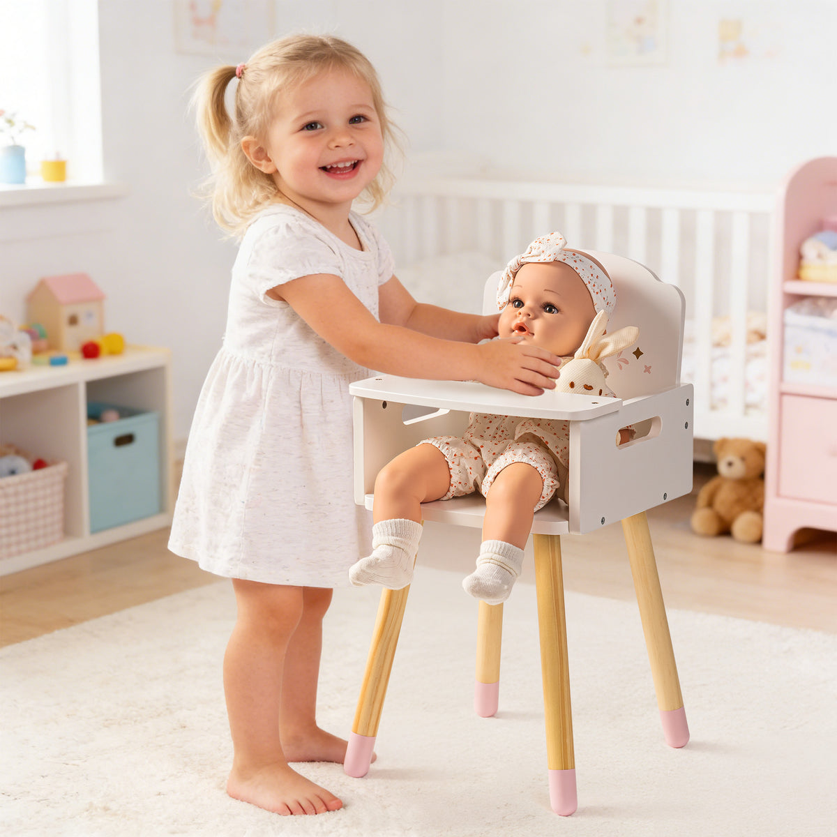 Smiling little girl seats her baby doll in the ROBUD white heart-back doll high chair in a bright nursery.
