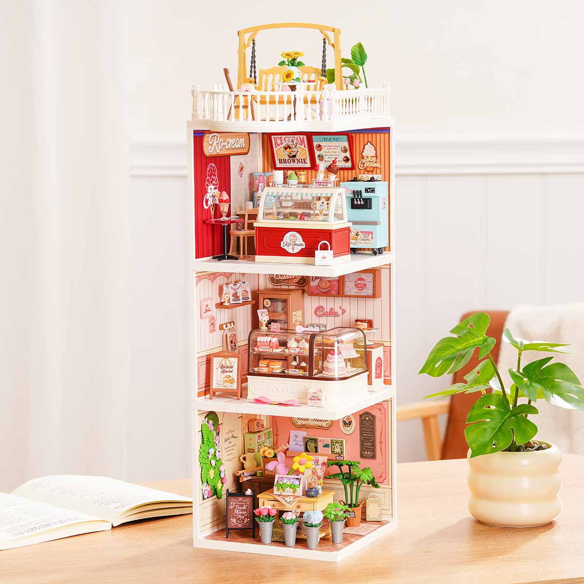 Rolife Super Creator Series 3-in-1 I Shape miniature tower with pink ice cream shop on top, cake bakery in the middle, and flower shop at the bottom on a wooden table.