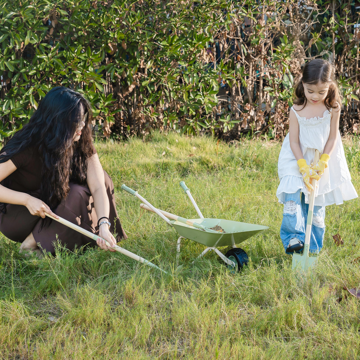 Mother and daughter gardening side by side outdoors using tools from ROBUD Kids Wheelbarrow Set on a grassy lawn