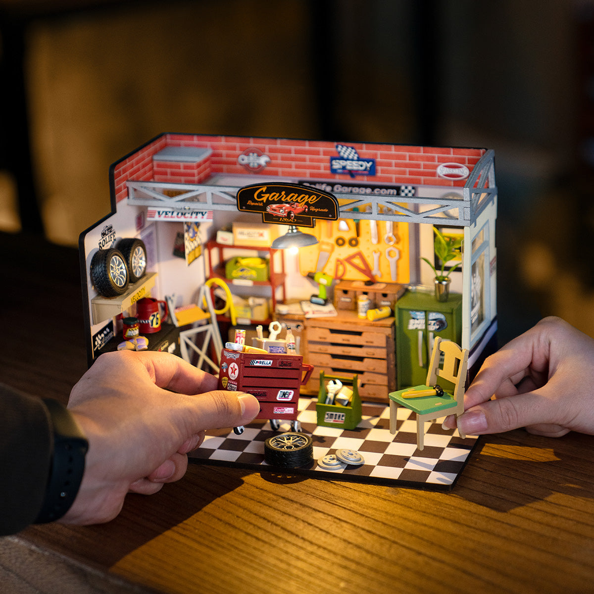 Official Rolife Garage Workshop miniature displayed on a table while two hands arrange its furniture