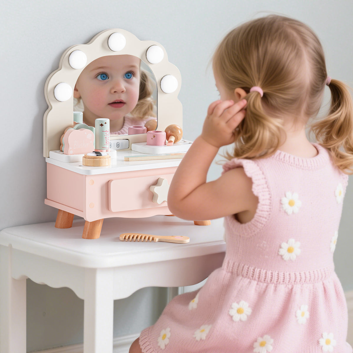 Girl in a pink floral dress gazes at her reflection in the lit ROBUD pink shell-arc wooden vanity with accessories nearby.
