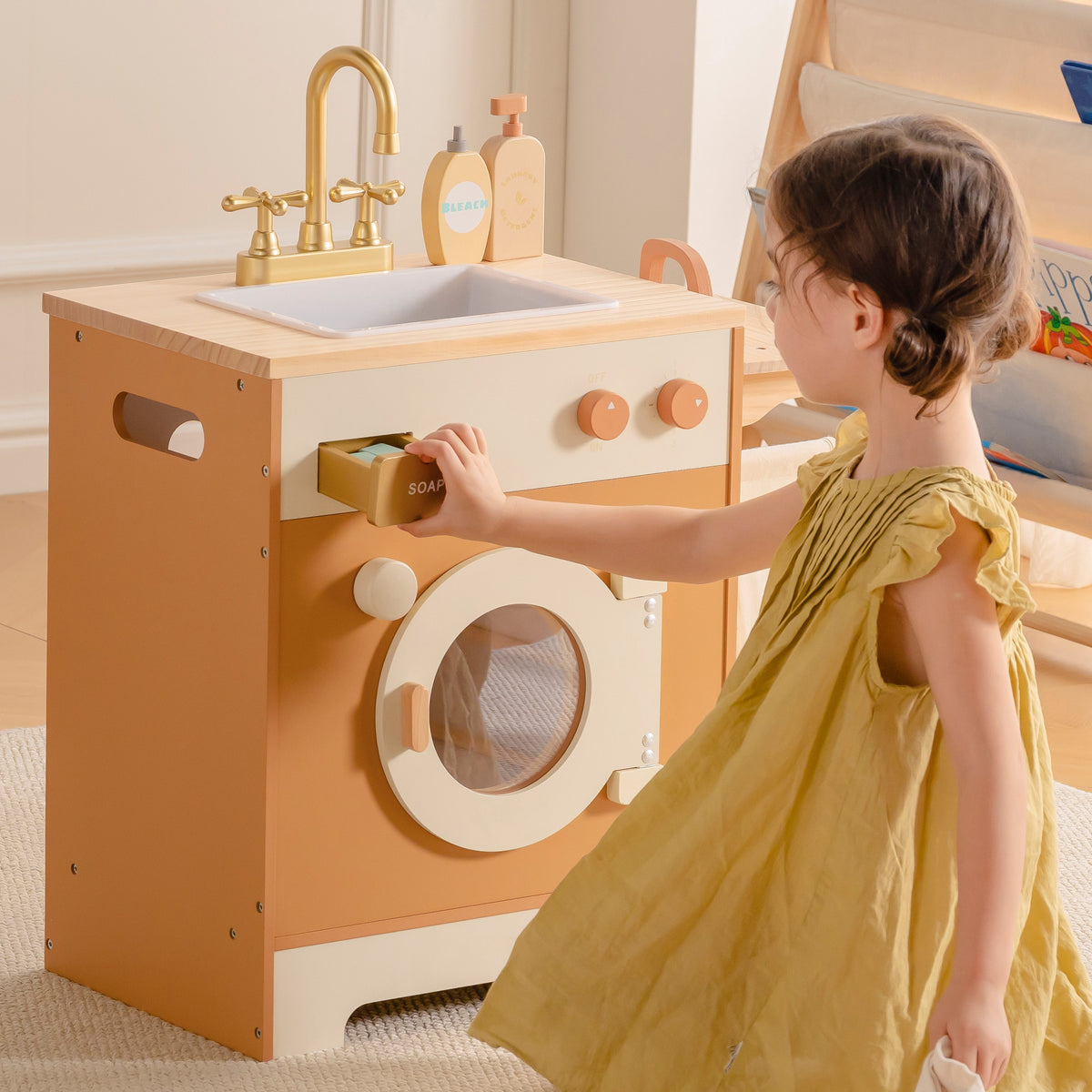 Toddler girl in yellow dress turning the dial on ROBUD Wooden Caramel Laundry Playset featuring integrated sink and washer