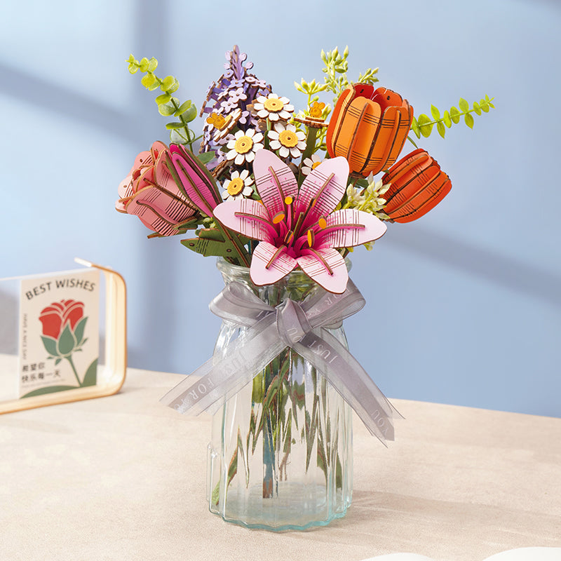 Rowood wooden flower bouquet arranged in a clear glass jar with a gray ribbon bow, featuring a pink lily, orange tulips, a purple flower, green leaves, and white daisies