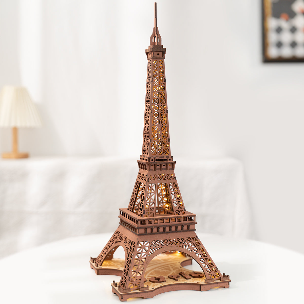Rolife Eiffel Tower wooden model fully illuminated with internal LED lights standing on a white surface in a softly lit room