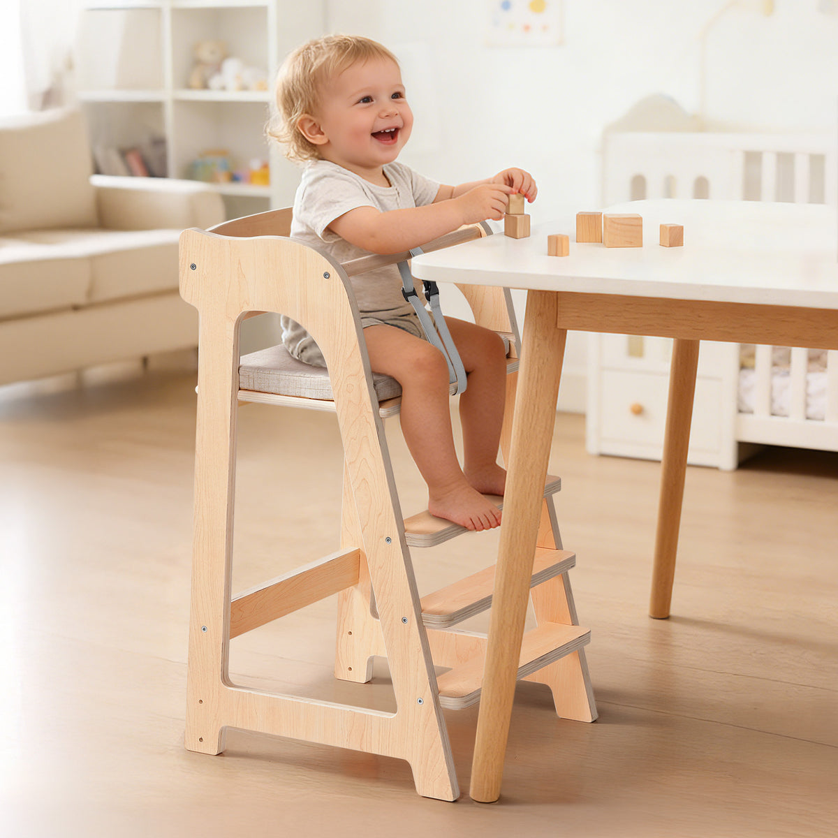Cheerful toddler sits in a ROBUD solid wood high chair with building blocks on the tray in a bright modern home.