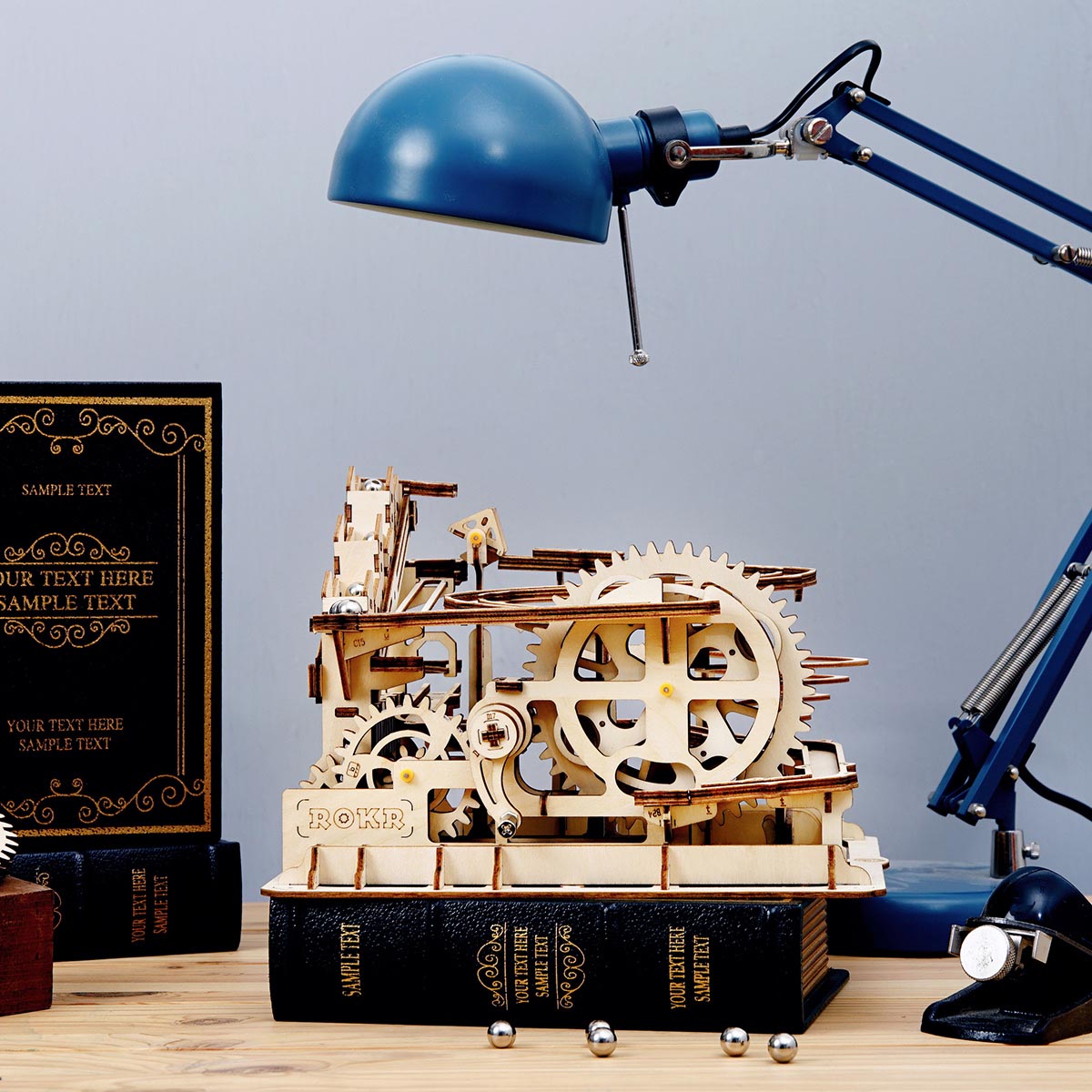 ROKR Marble Parkour marble run on stacked books beside a blue desk lamp in warm wooden tones