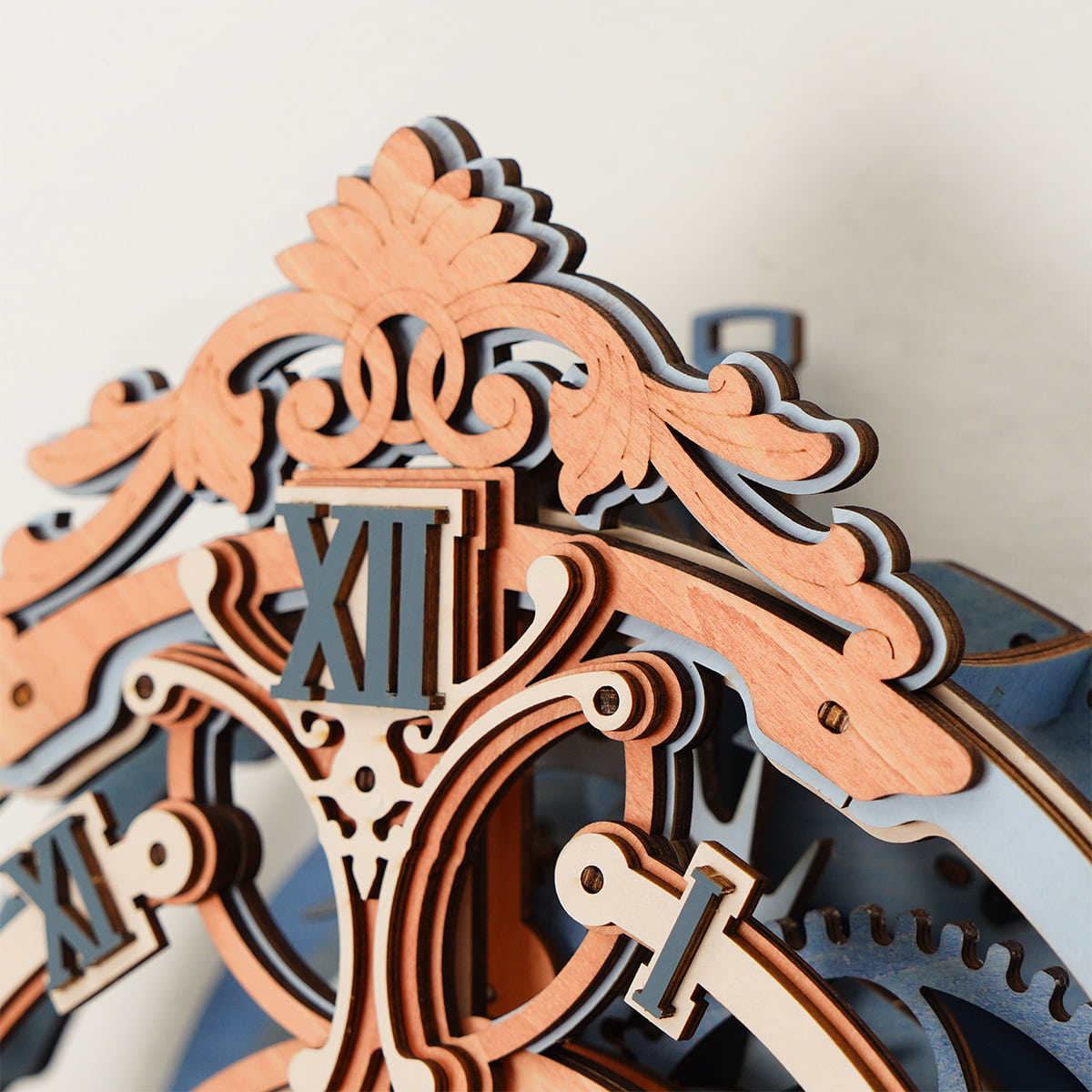 Upper section of the ROKR Romantic Note Wall Clock showing Roman numeral XII and baroque carved wooden scrollwork in tan and slate blue