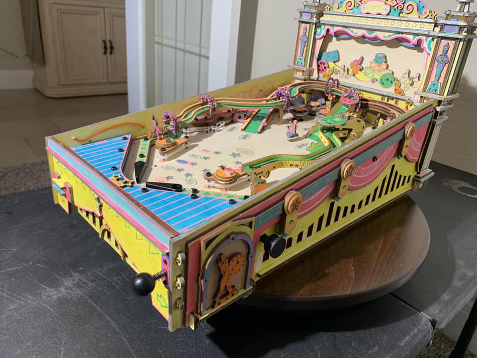 Robotime carnival pinball table sits on a round table with pastel sides and raised backboard.