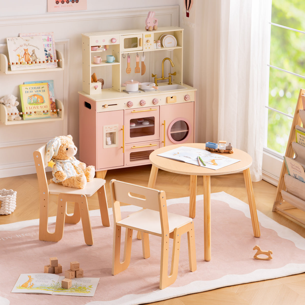 ROBUD Glowwood white and natural wood table set paired with the pink kitchen unit seen from across the playroom.
