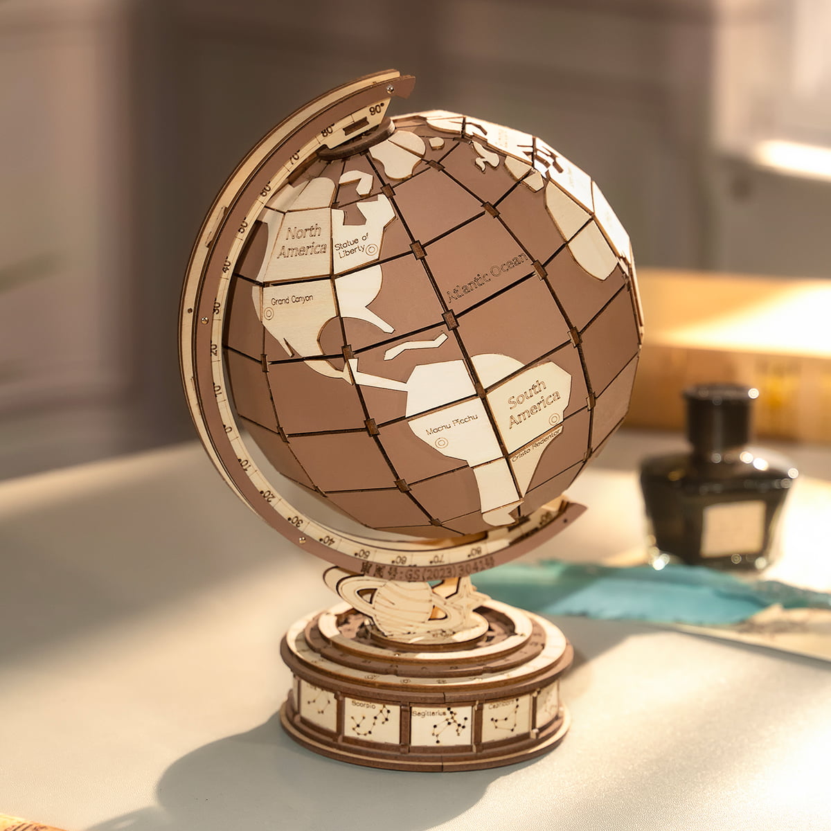 Wooden globe puzzle with engraved continents resting on a decorative carved base beside a glass ink bottle in warm studio light