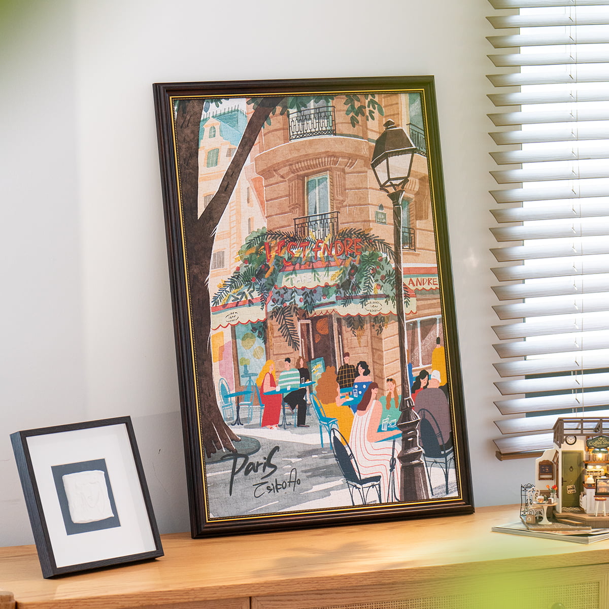 Rolife Leisure in Paris PT004 completed puzzle framed and displayed on wooden shelf beside smaller photo frame by a window