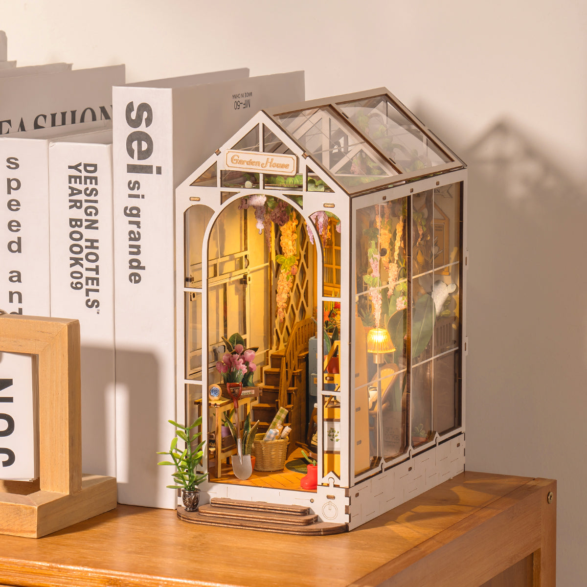 Rolife arched greenhouse book nook with plants and illuminated interior on bookshelf beside picture frame