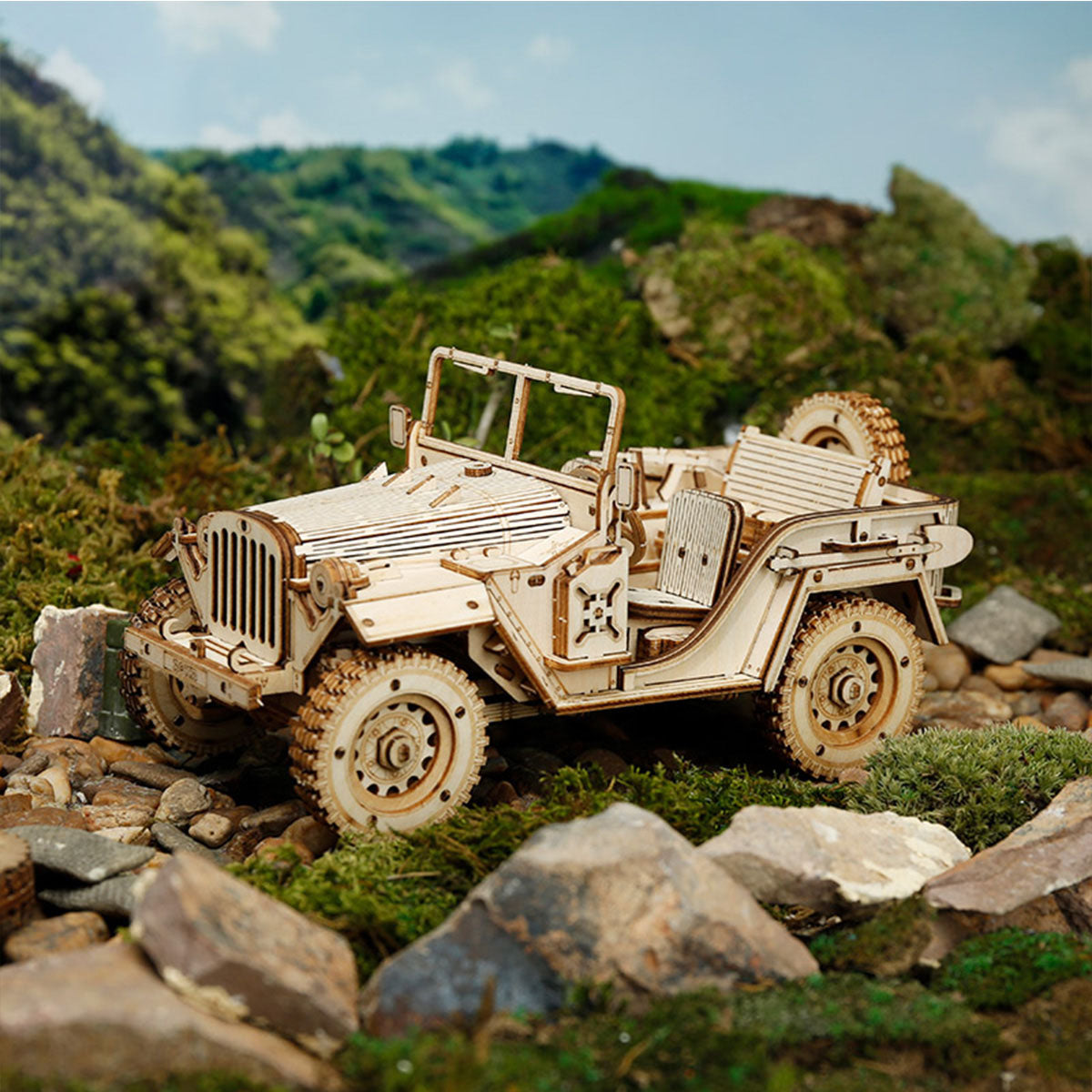 ROKR Army Jeep wooden scale model rear three-quarter view on rocky terrain with rolling green hills