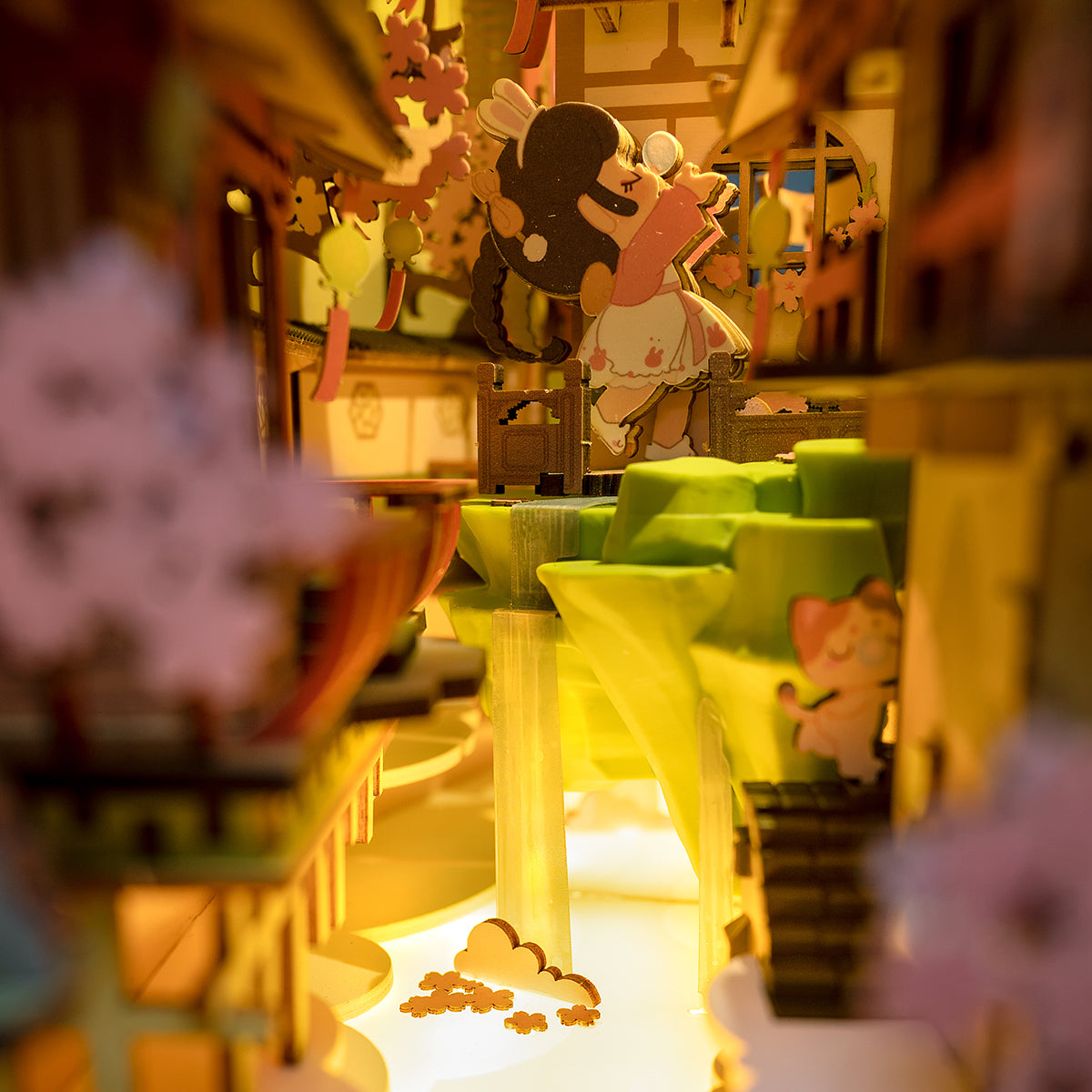 Rolife Falling Sakura book nook interior close-up with warm amber lighting, green terraced steps, scattered petal details and a tiny figure