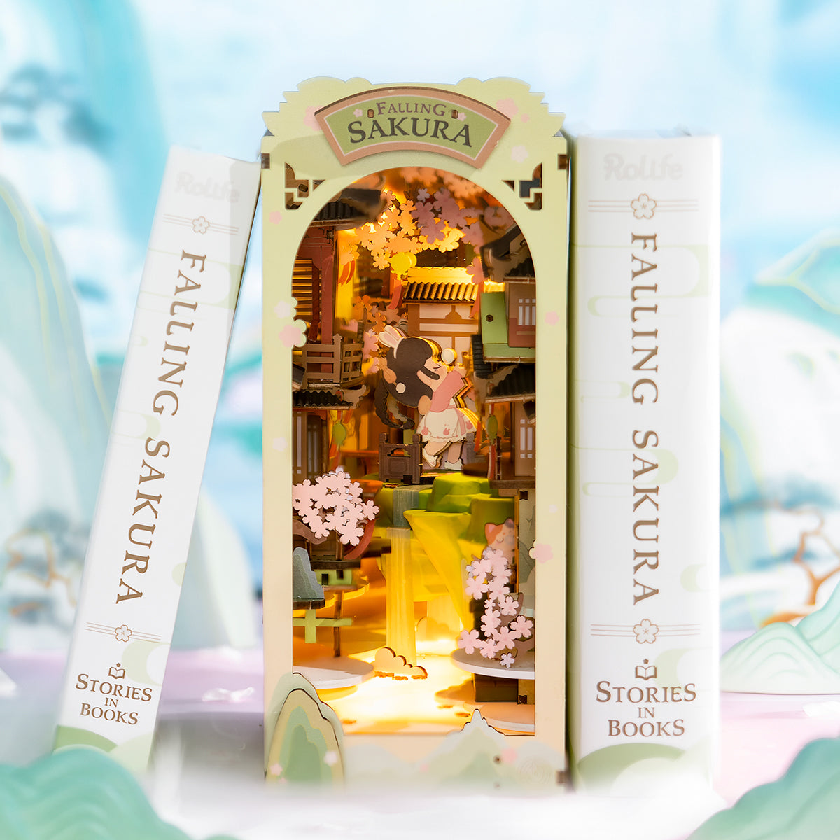 Rolife Falling Sakura book nook standing between two books with warm glowing interior showing cherry blossom trees and wooden pagoda scene