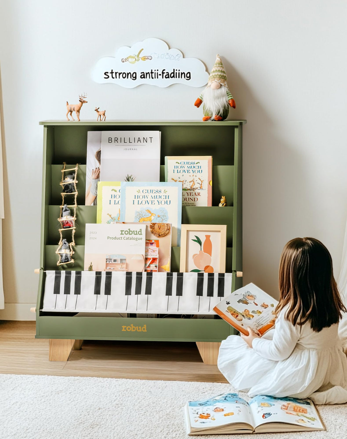 A girl reading a book on a rug beside the ROBUD Wooden Kids Bookshelf Piano green version filled with picture books and an art print in a bright home interior with a gnome plush on top