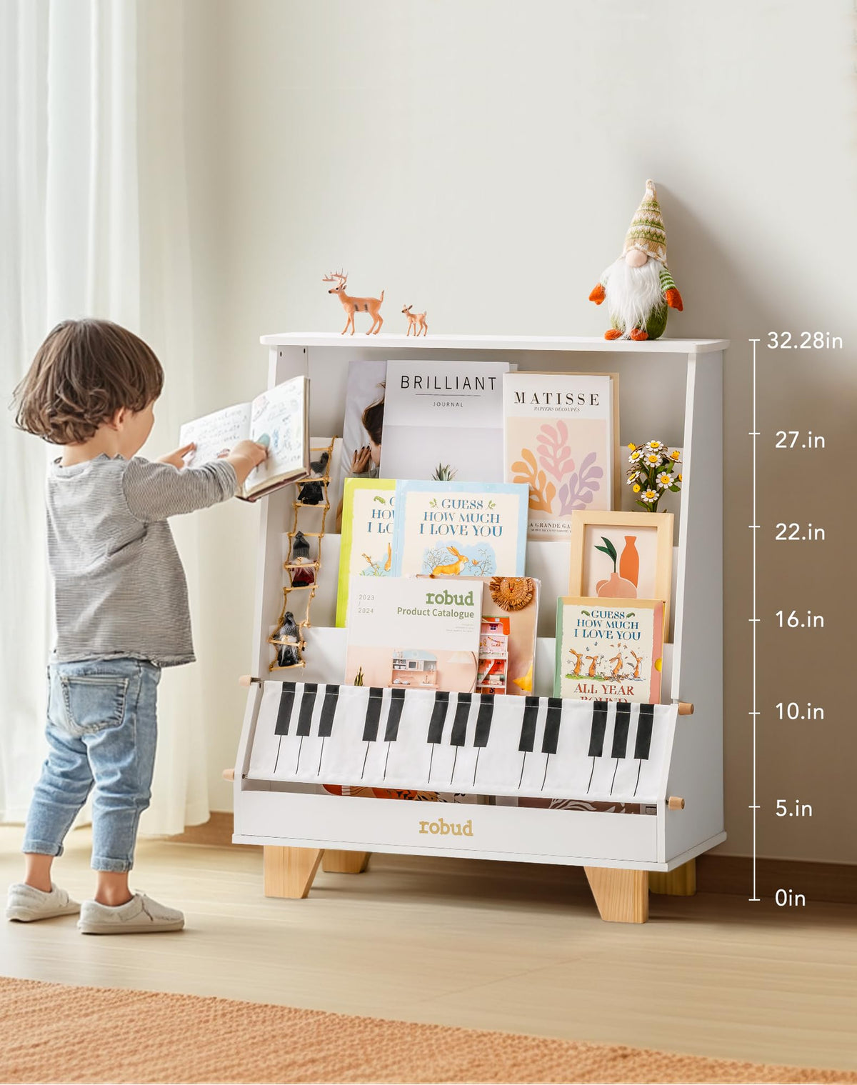ROBUD Wooden Kids Bookshelf Piano white with a young child reaching up to take a book from the shelves loaded with colorful picture books and art prints in a bright natural light room with height markers