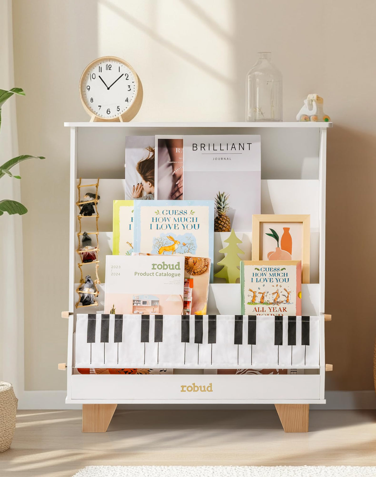ROBUD Wooden Kids Bookshelf Piano white version in a warm cozy room with a round clock and glass bottle on top in a natural-light lifestyle setting showing books and decorative gnome figure on the shelf