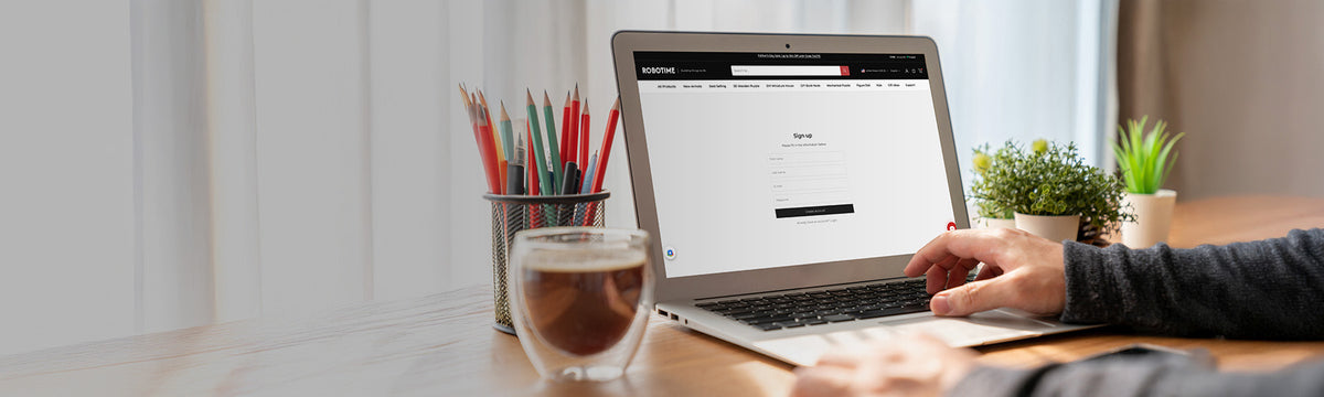 Robotime Online signup page shown on a laptop screen in a cozy home workspace with pencils and a coffee cup on the desk.
