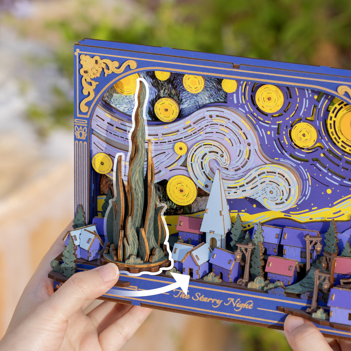 Rowood The Starry Night Wall Art 3D Wooden Puzzle TH003 hand holding the puzzle outdoors, showing the cypress and village layers on the left half with star gears visible