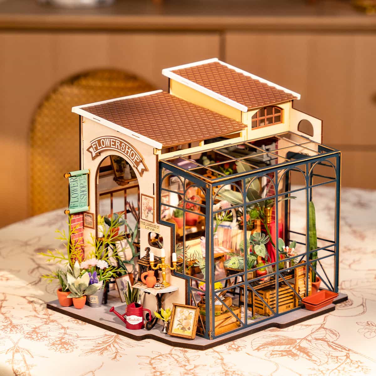 Rolife Emily's Flower Shop DG145 miniature house rear angle view showing the blue greenhouse wing, Flower Shop signage and warm interior LED glow on a marble table
