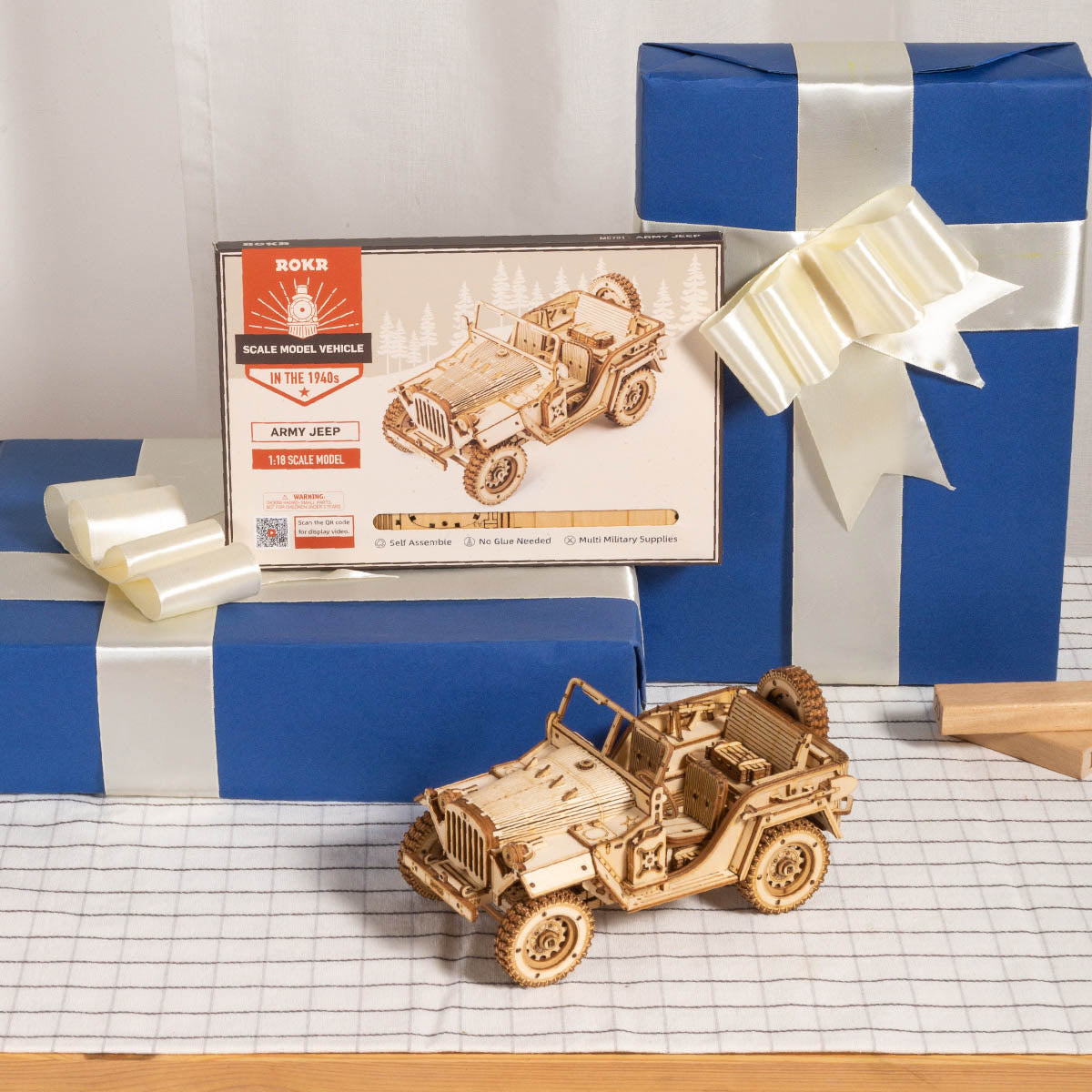 ROKR Army Jeep completed wooden model beside blue gift box with ribbon bow on graph paper surface