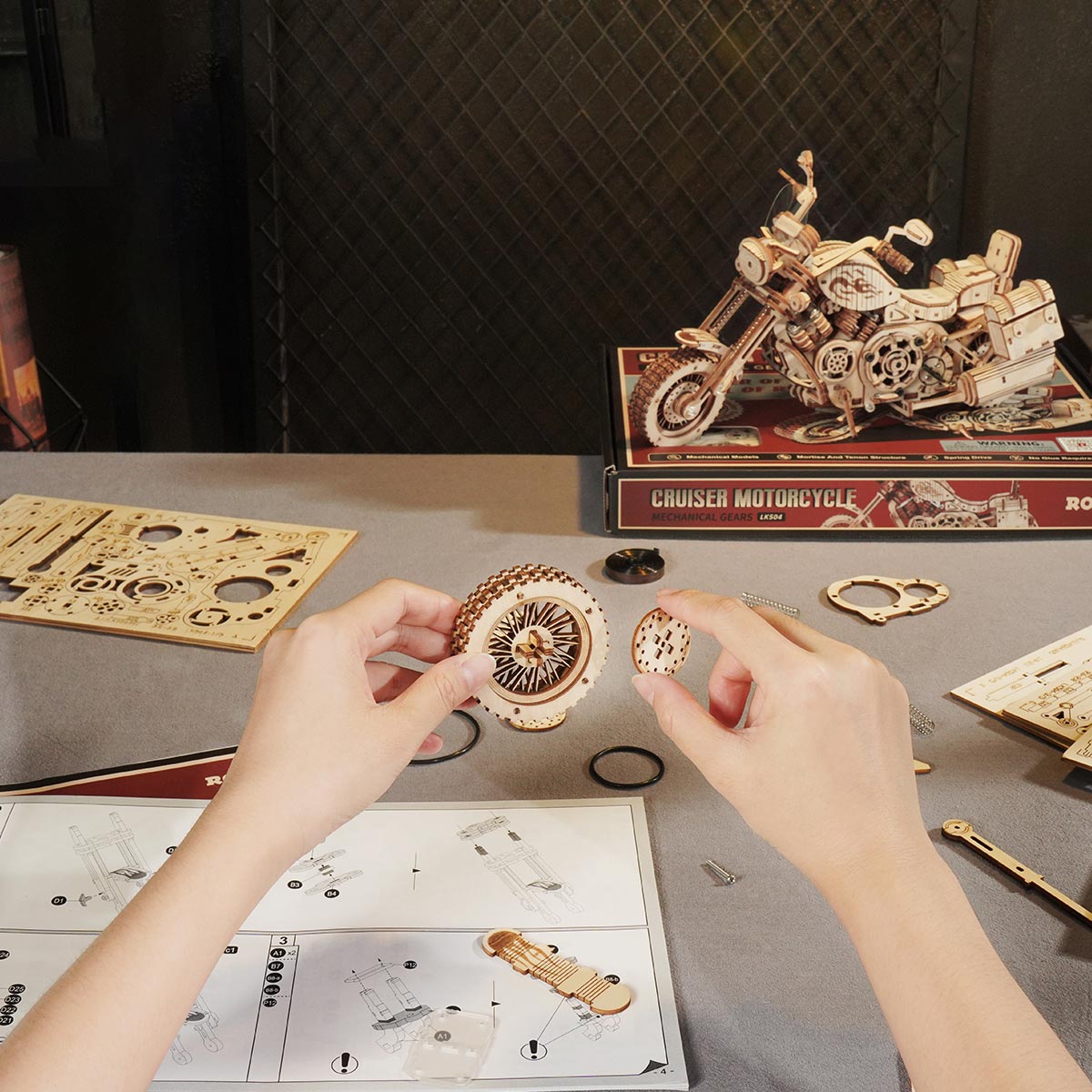 Hands assembling ROKR Cruiser Motorcycle wooden puzzle pieces at a desk with instruction sheet nearby