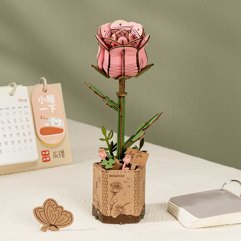 Rowood wooden pink rose stands in a cork style base with packaging and small desk props.