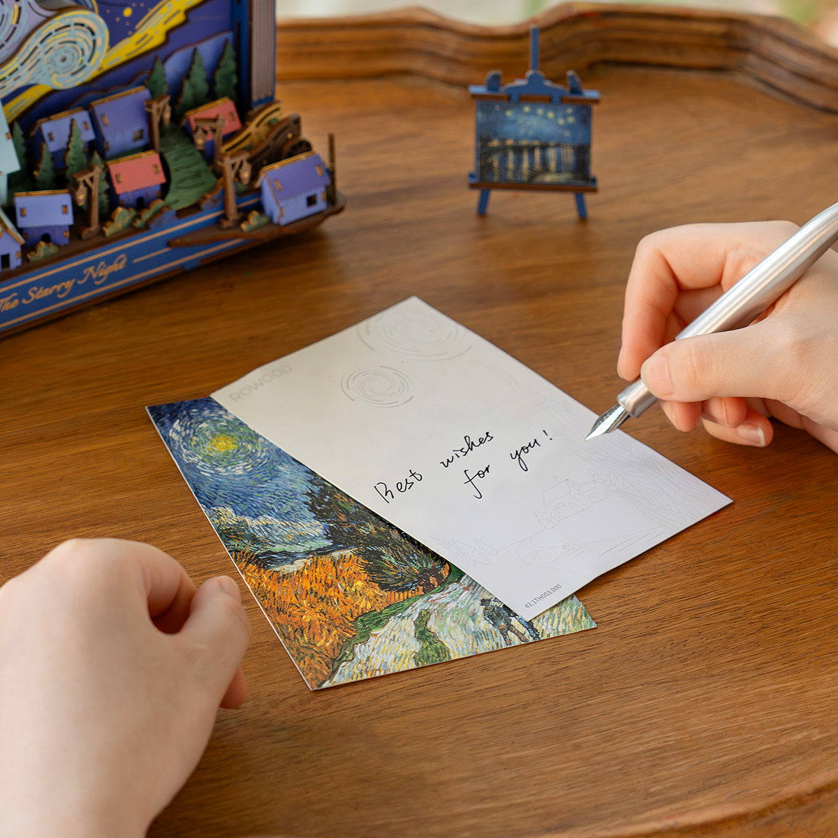 Rowood The Starry Night Wall Art 3D Wooden Puzzle TH003 hands-on lifestyle, person placing the wooden cypress tree piece into the lit puzzle on a wooden surface with scattered components