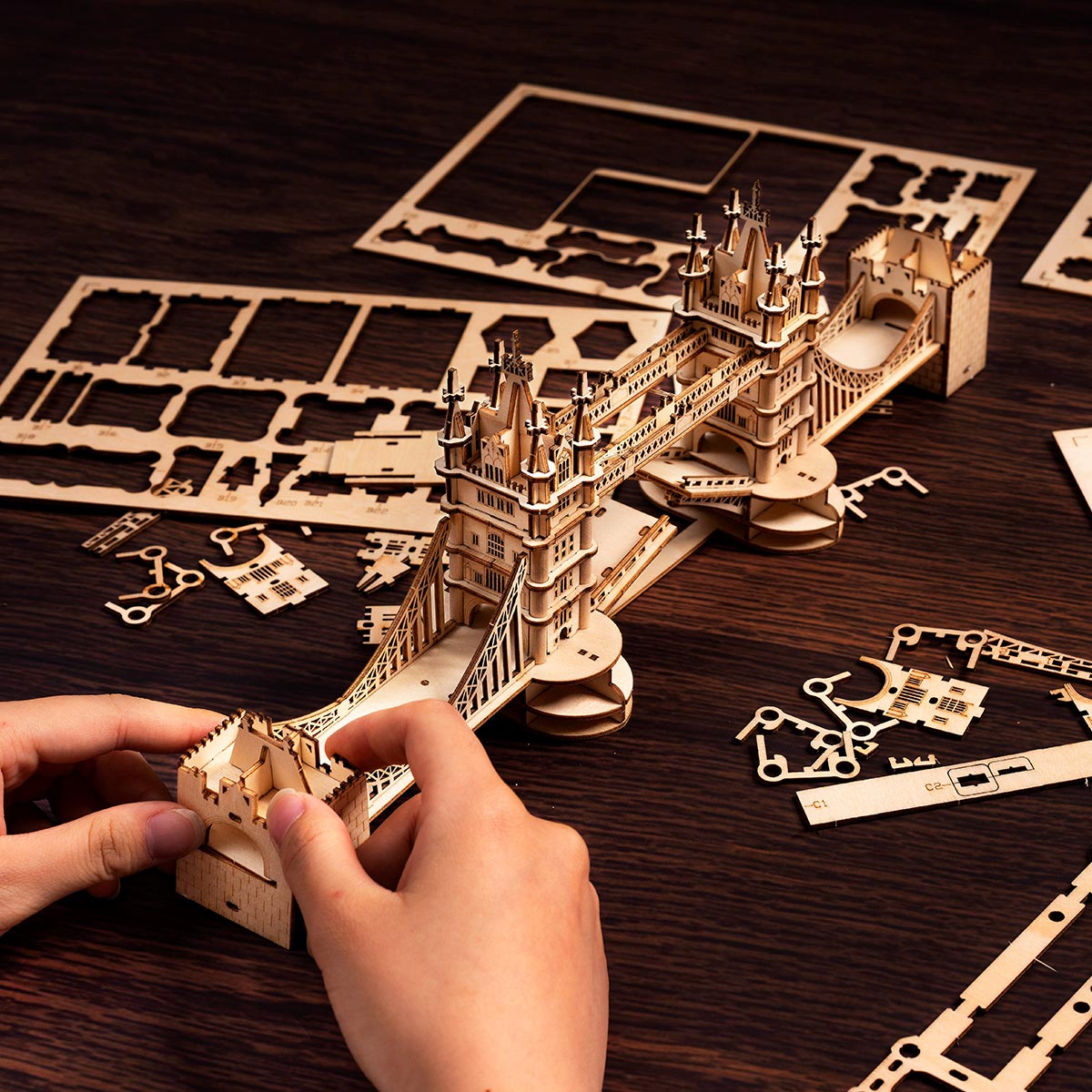 Hände beim Zusammenbau des Rolife Tower Bridge Holzpuzzles mit lasergeschnittenen Sperrholzplatten auf einem dunklen Walnusstisch