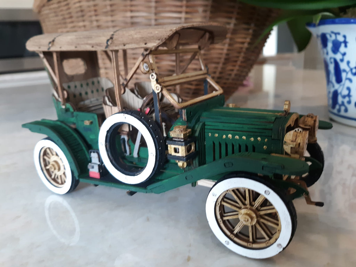 Green vintage car model with white tires and tan seats displayed on a light tabletop.