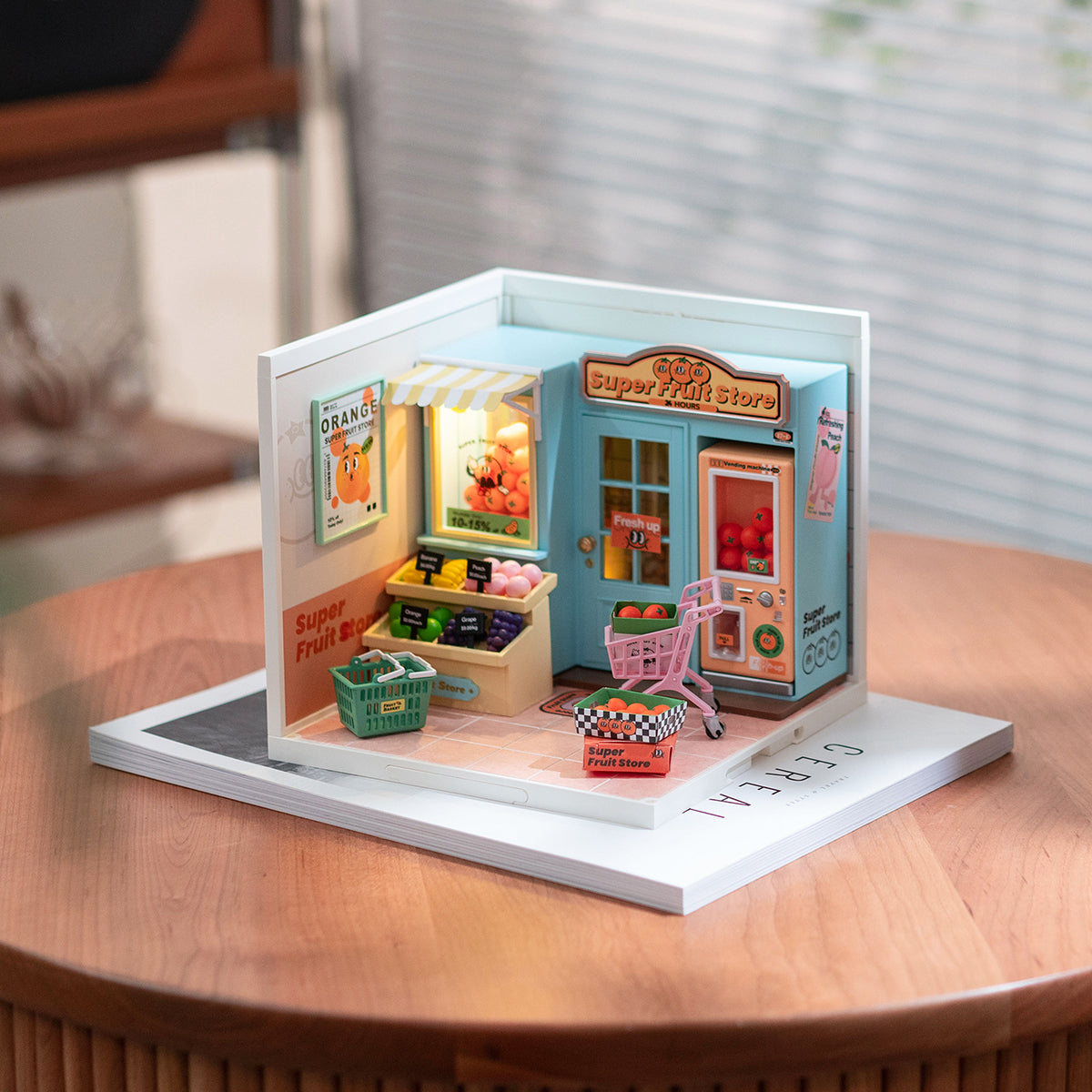 Rolife Super Fruit Store DW003 miniature displayed on a wooden round table with a magazine, showing the blue and pink