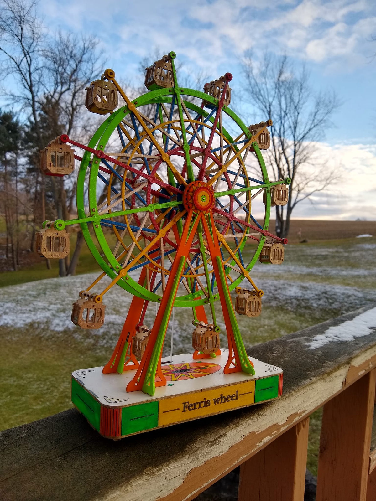Robotime Ferris wheel model stands outdoors with colorful spokes under a blue sky.