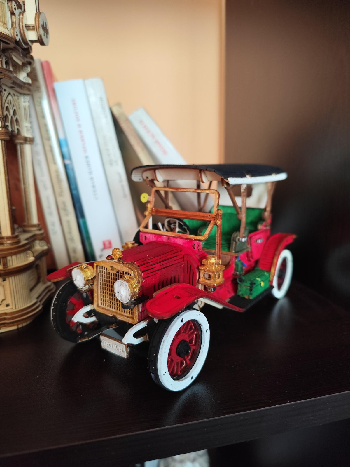 Red vintage car model with green wheels and detailed seats displayed on a dark shelf.