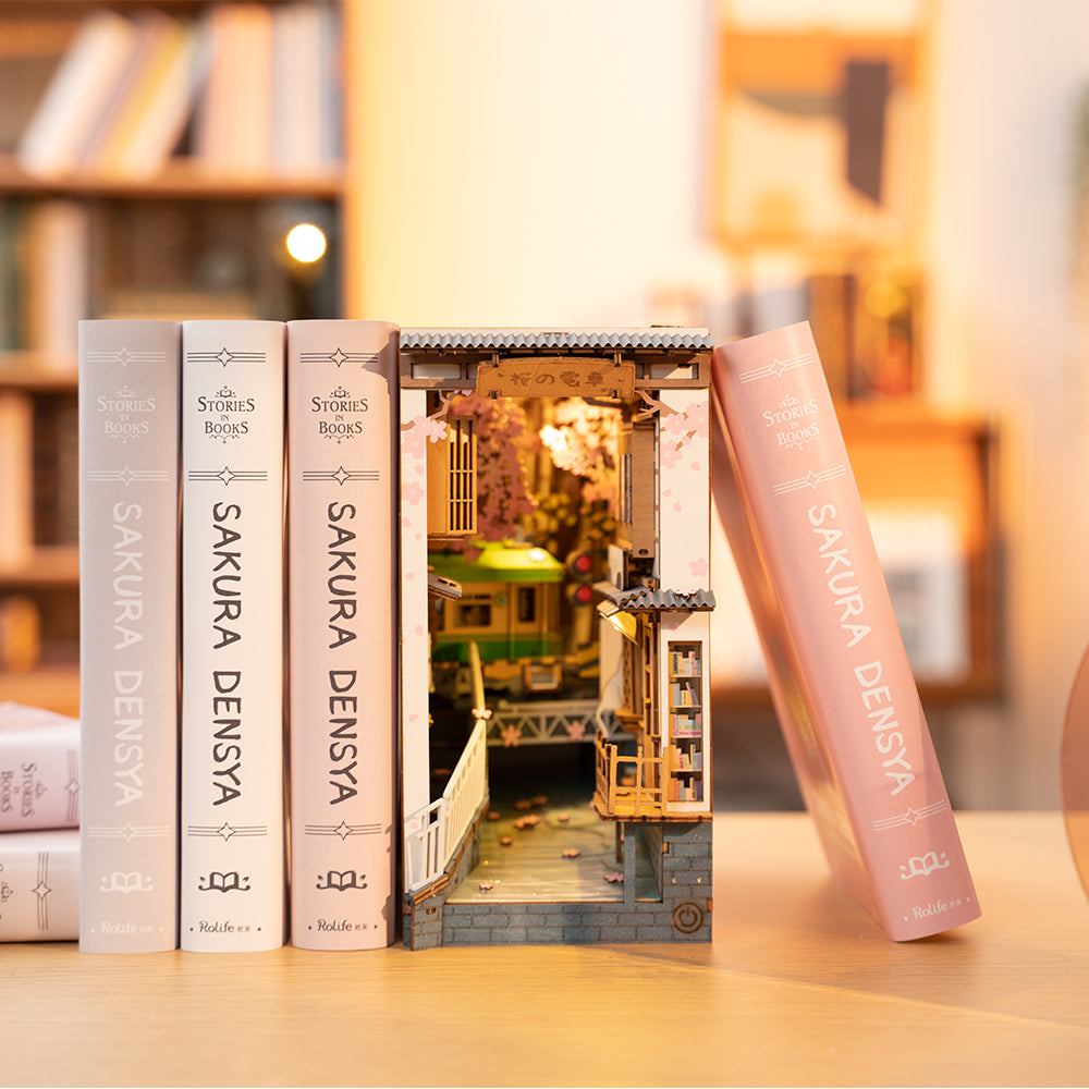 Rolife Sakura Densya TGB01 nestled between pink and cream books on wooden shelf as functioning book end