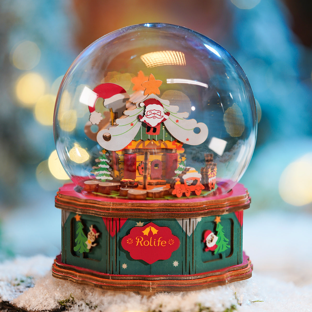 Rolife Christmas Snow Globe AM46 glowing on snow with lit interior showing Santa on rooftop reindeer and Christmas tree under glass dome