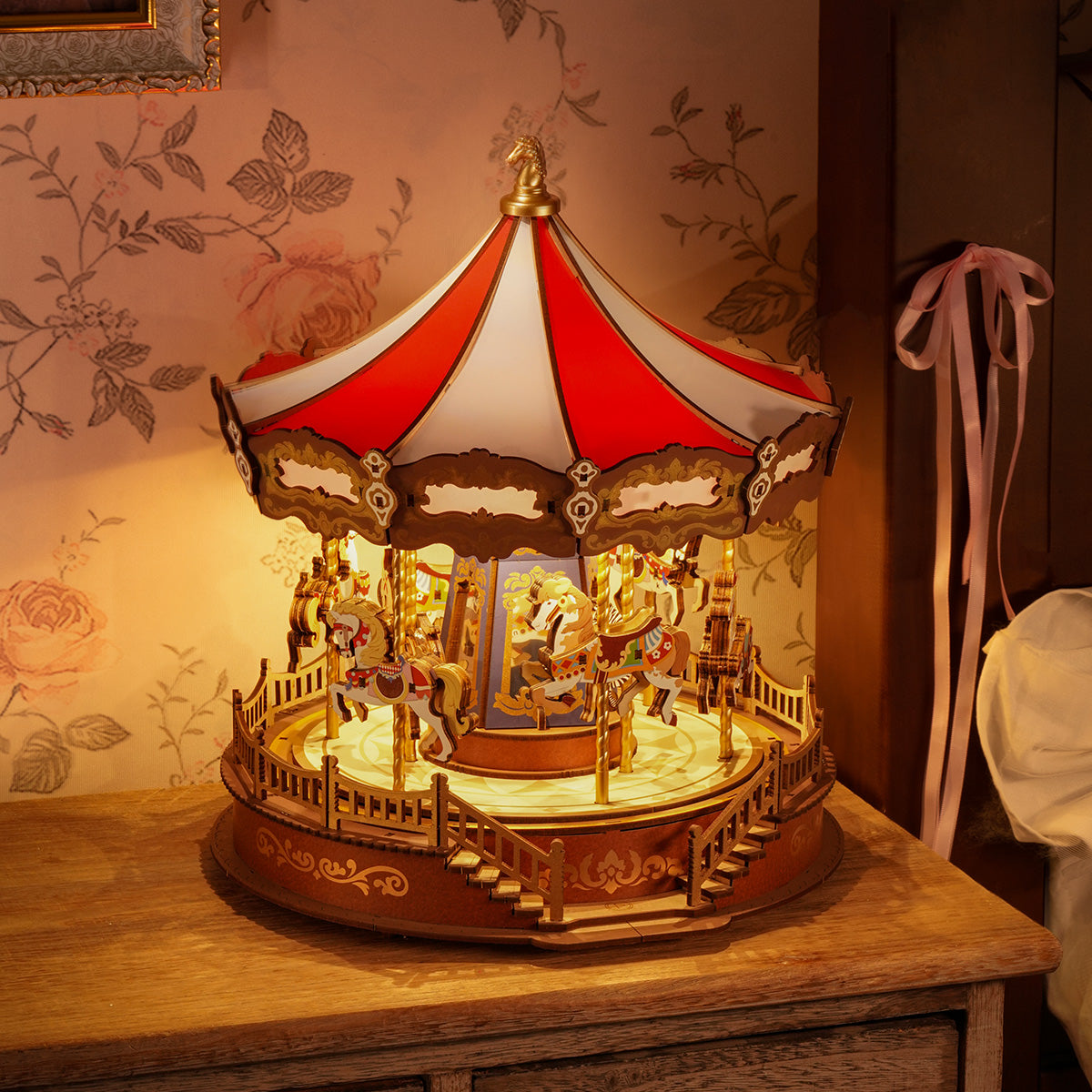 Rolife Classic Carousel AMC01 Music Dreamer glowing with warm LED lights in a vintage floral wallpaper room setting on wooden dresser