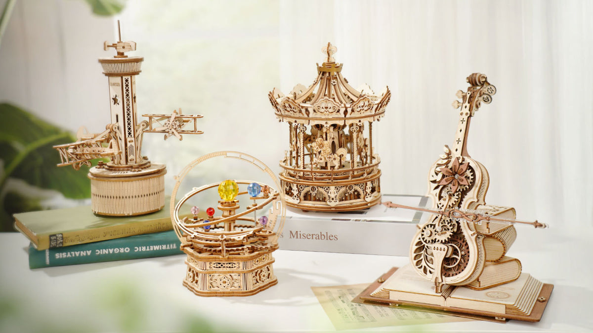 ROKR Magic Cello Mechanical Music Box AMK63 lifestyle collection banner showing four natural-wood music boxes on a white surface near a bright window